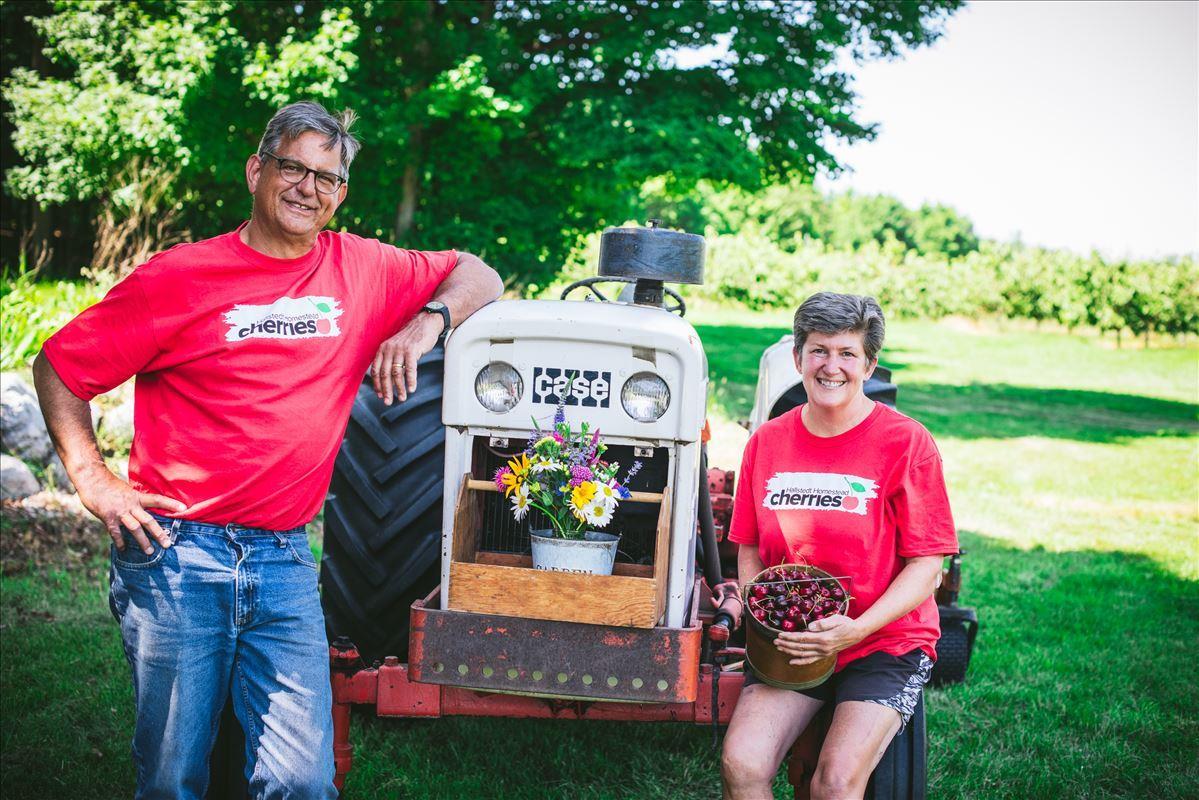 Sarah and Phil Hallstedt in front of tractor at their u-pick cherry farm in Northport