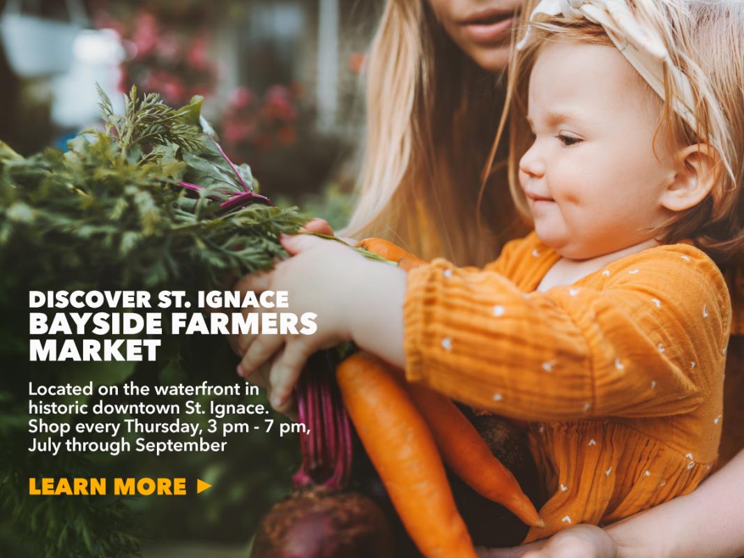 Little girl holding carrots in Bayside Farmers Market in St. Ignace